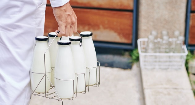 PXL_20230507_142535864 hand holds mini-crate of six old-fashioned milk bottles near front doorstep