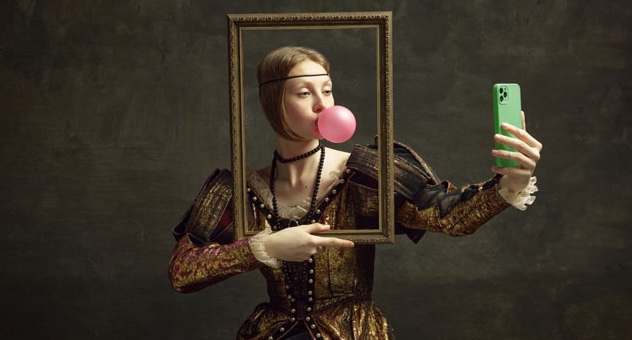 elizabethan_woman_selfie_portrait_opt_shutterstock person in Elizabethan dress holding picture frame around their face blows bubble with gum and takes selfie on mobile phone