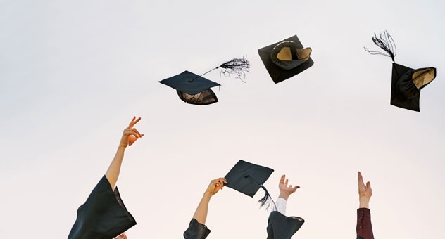 Arms of students in graduation gowns reach into sky throwing tasselled caps in the air