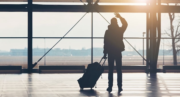 Figure in silhouette with suitcase waves plane off at airport