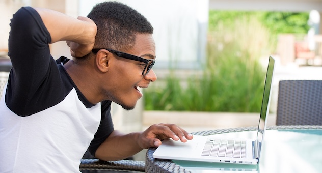 PXL_20230507_142535864 Smiling preppy guy in glasses leans over laptop, holding a hand to the back of his head