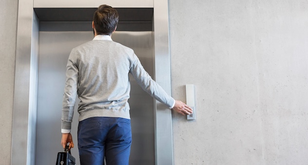 man_calls_elevator_opt Person in casual businesswear with briefcase seen from behind, pressing the button for an elevator