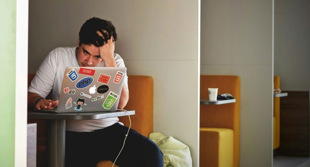 man_at_computer_unsplash Stressed person with head in hands sitting in cafe booth and looking at laptop