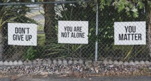 Series of rectangular signs attached to chain-link fence: don't give up, you are not alone and you matter