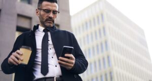 Businessman in street holds coffee and checks iphone
