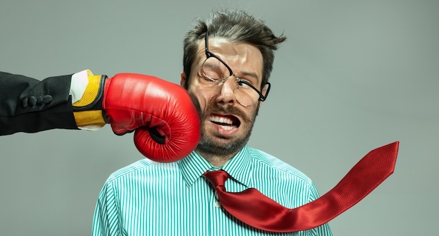 Business man grimacing as boss wearing boxing glove punches him in the face