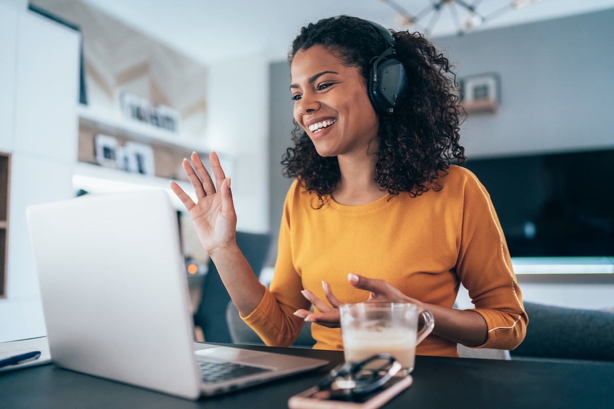 Professional woman, working remotely, smiles and gesticulates at her screen.
