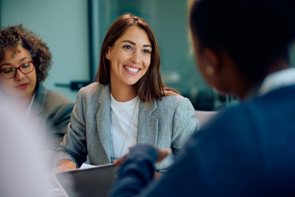 Professional young woman smiles confidently at meeting attendee, while referencing a document in an open folder