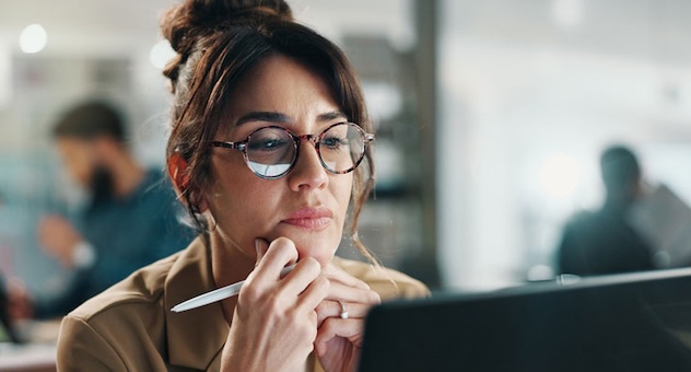Professional in office intently reading something on computer screen, which is reflecting off their glasses